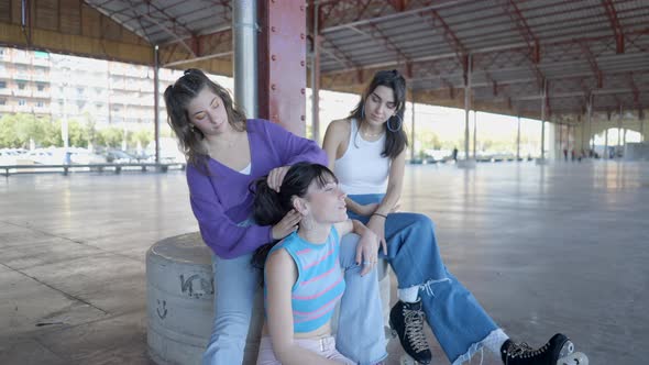 Roller Skater Girls in Colorful Clothes Sit Outdoors and Fix Hair alt