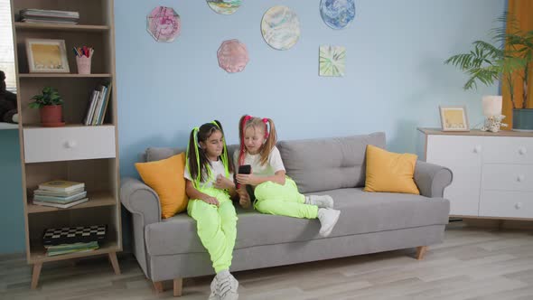 Children Entertainment Trendy Friends on Sofa Share Video to Social Media Little Girls Use Mobile alt