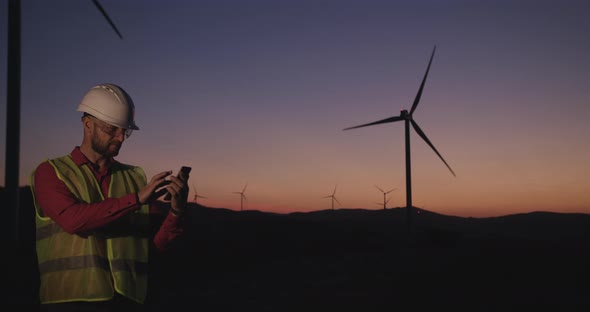 The Young Engineer Pulls Out a Phone with Information and Then Looks at the Camera. Sunset alt