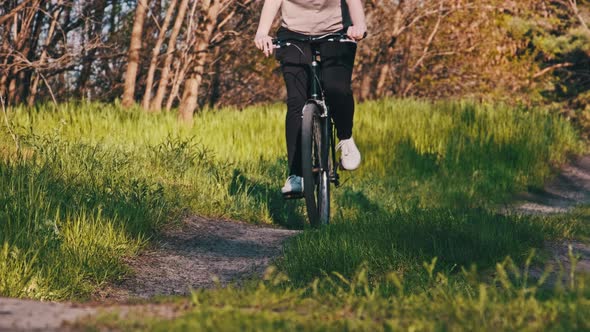 Young Woman on a Bicycle Rides Along Green Forest Path in Sunny Summer Day alt