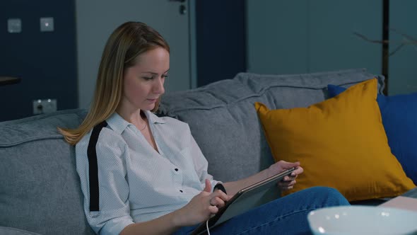 Young Woman Sitting on Sofa and Using Tablet