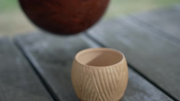Closeup Clay Cup with White Milk Pouring From Pot in Slow Motion alt