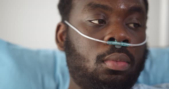 Close Up of Young African Man Patient with Nasal Cannula Resting in Bed at Hospital alt