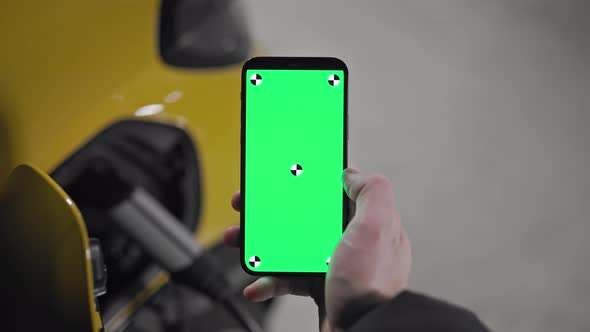 Slow motion green screen smart phone being held with electric car charging