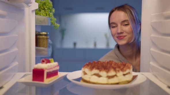 Sweet tooth woman in bathrobe at midnight opening refrigerator and cant stop eating sweet desserts