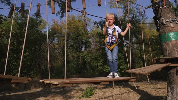 Little Boy with a Safety Carbine Goes on a Rope on the Background of Forest alt