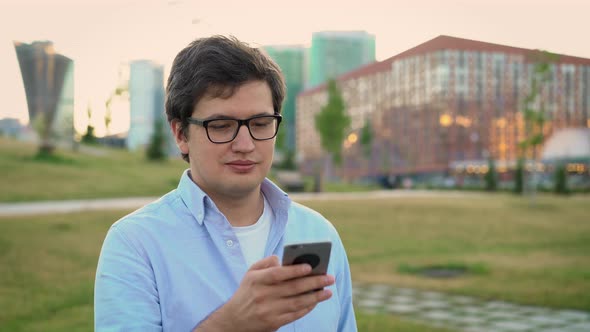 Portrait of Adult Man Using Mobile Phone on Background of Park Lawn