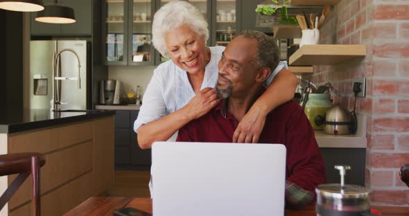 Senior African American husband and mixed race wife happily working on a laptop at home alt