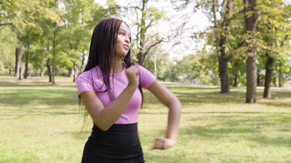 A Young Black Woman Dances with a Smile in a Park on a Sunny Day alt
