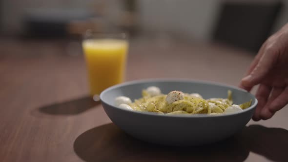 Slow Motion Man Put Pesto Fettuccine with Mozzarella in Blue Bowl on Walnut Table alt