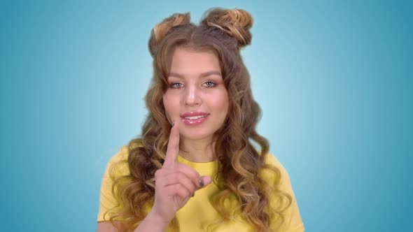 Beautiful Young Girl in a Yellow Vest Puts a Finger to Her Lips and Shows a Gesture of Silence and alt