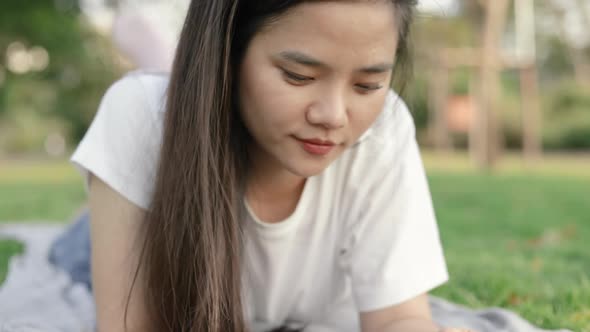 Female using smartphone shopping online and chatting with friends while lying on the floor grass.