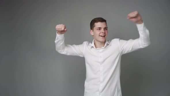 Cheerful Dancing Guy in a White Shirt on a Gray Background