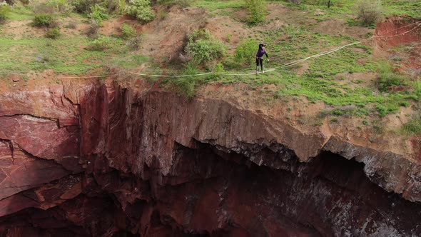 A Man Is Turning Around and Balancing on the Tightrope Over a Huge Pit alt