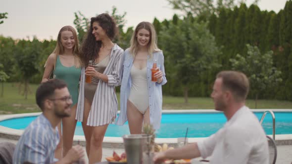 Group of happy young people cheering with drinks and eating fruits by the pool in the garden