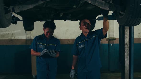 Two professional car mechanic using paperwork makes the oil and engine check to the car.