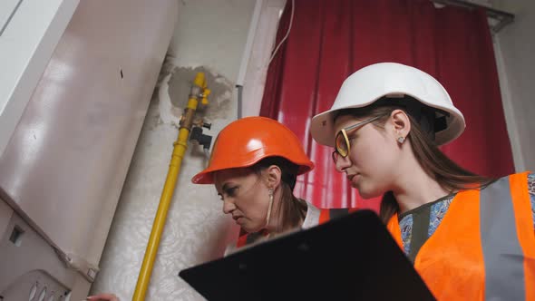 Two Women Checker Checking Technical Data of Heating System Equipment in a Boiler Room alt