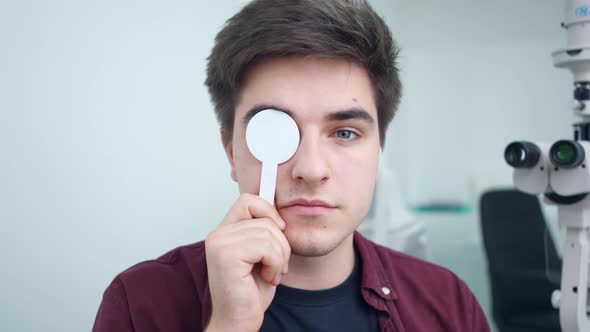 Front View Man Closing Eyes One By One with Eye Occluder Looking at Camera alt