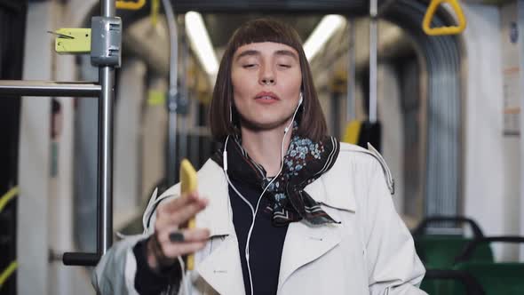 Portrait of Young Happy Woman Wearing in Coat with Headphones Listening To Music and Funny Dancing