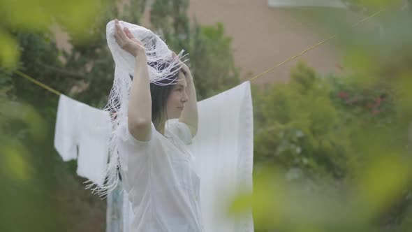 Attractive Mature Woman with Long Hair Removing White Clean Shawl From the Clothesline alt