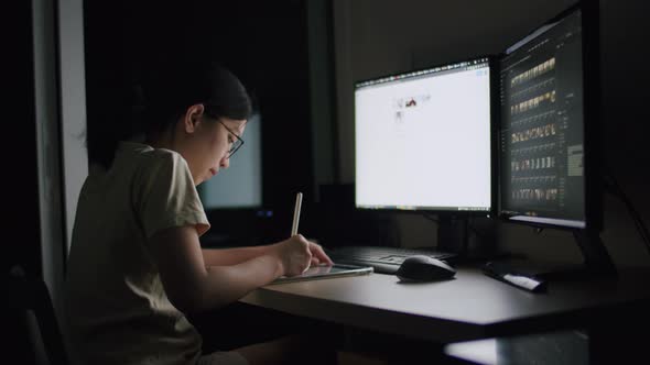 A young woman using a tablet at night in a home office.