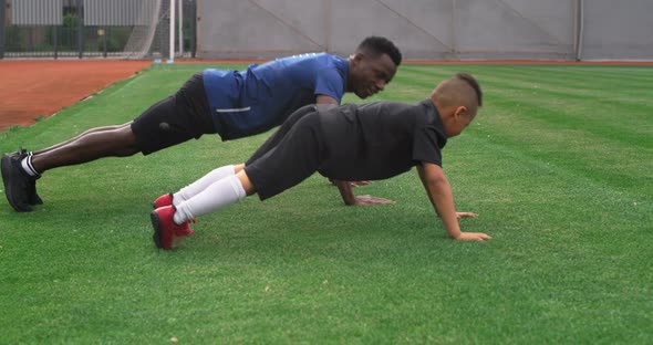 Diverse Trainer and Boy Doing Push Ups on Field alt