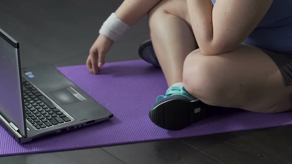 Teenager Watching Video on Laptop on Floor, Tapping Fingertips Against Yoga Mat alt