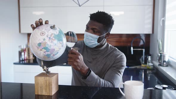 Young Black Man with Face Mask Looking at the Through Magnifying Glass. Travel Ban During Global alt