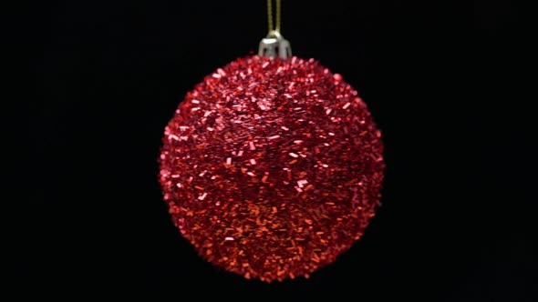 Close-Up View of Shiny Bright Red Christmas Ball Rotates on Axis, Hanging on Black Background