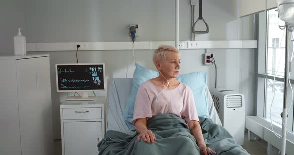 Ill Mature Woman with Nasal Cannula Sitting in Hospital Bed alt