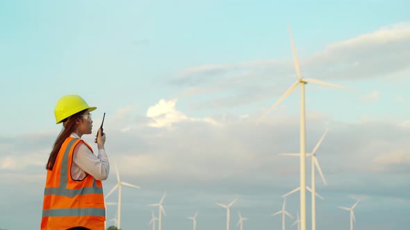 young female engineer using walkie talkie to checking system against wind turbine farm