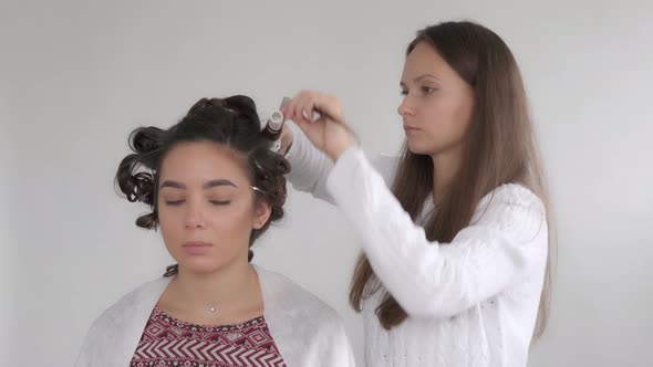A hair stylist makes a hairstyle for a young beautiful girl with long dark hair alt