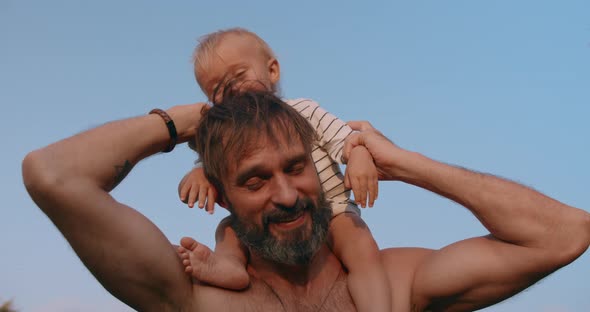 Smiling Baby Boy Sits on Fathers Neck and Have Fun Together Outdoor in Sunset alt