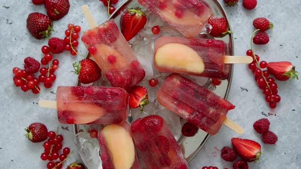 Homemade Raspberry Strawberry Apple and Currant Popsicles on Metal Plate with Ice Assorted Berries