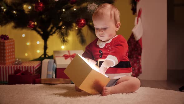 Cute Baby Boy in Santa Costume Looking Inside Christmas Present Box alt
