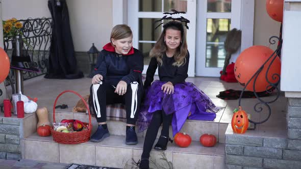 Wide Shot Two Happy Kids Singing and Dancing Sitting on Front Yard Porch on Halloween alt