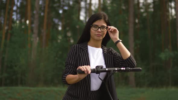 Confident Business Woman Standing with Electric Scooter and Looking at you alt