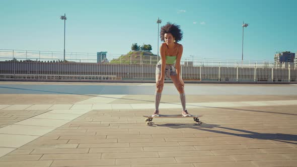 Beautiful young woman cruising around the city with her longboard. alt