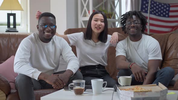 Three Positive Multiethnic Friends Posing in Living Room Sitting on Comfortable Couch alt
