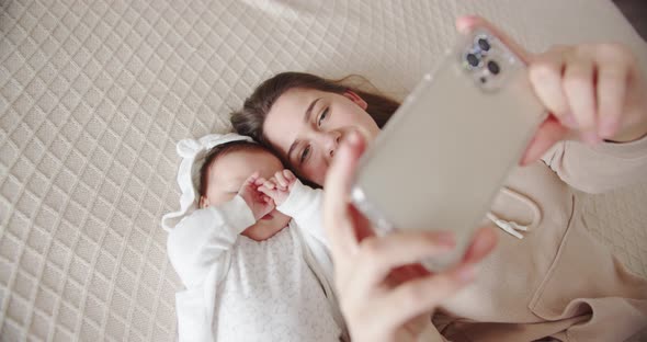 Mom Lies On The Bed With The Baby And Takes A Selfie On The Phone