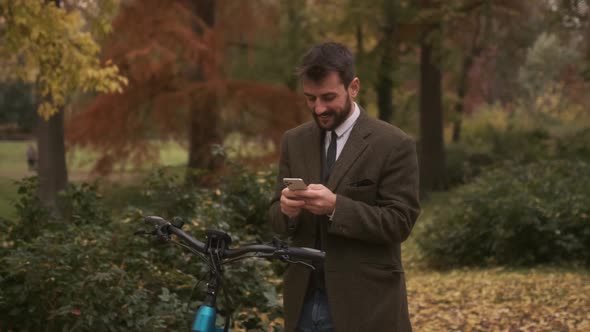 Handsome young man with electric bicycle using mobile phone in the autumn park