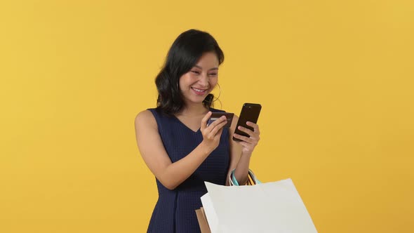 Asian woman carrying bags and using credit card for shopping online