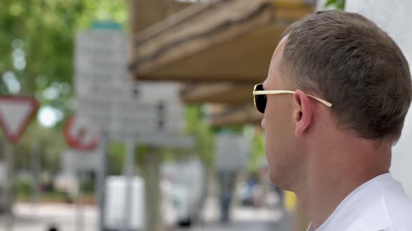 Young attractive man in sunglasses stands on the street and watches alt
