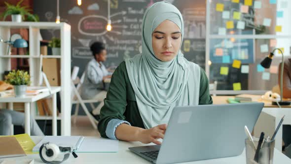 Portrait of Successful Muslim Woman in Hijab Working with Laptop Typing at Desk alt