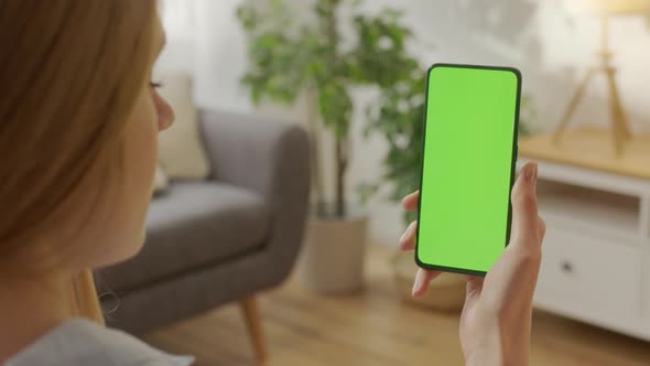 Back View of Woman at Living Room Sitting on a Chair Using Phone With Green Mockup Screen Chroma Key alt
