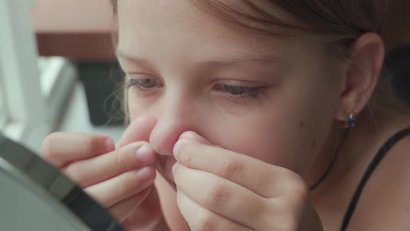 Young girl is trying to squeeze out pimple on her nose. Rash on face in adolescence. alt
