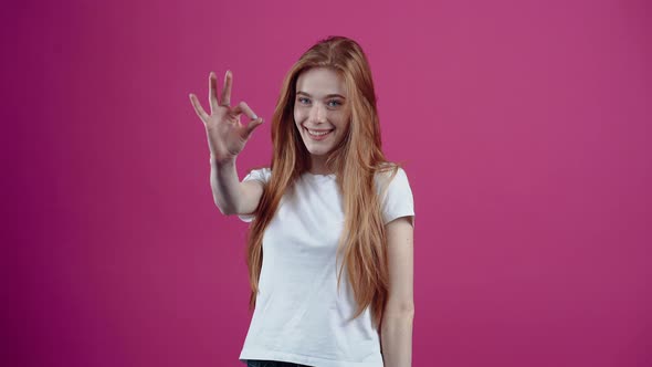 The Excited Redhaired Girl Cheerfully Shows the Ok Sign Delighted and Brings It Playfully to Her alt