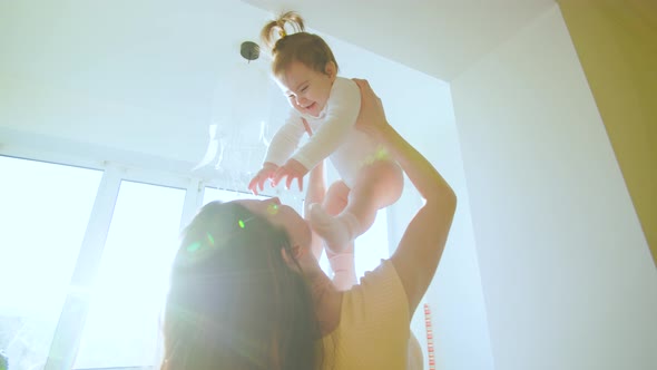 Caucasian Mom is Lifting Her Toddler Baby Girl High Up and Playing in the Sunlight at Home alt