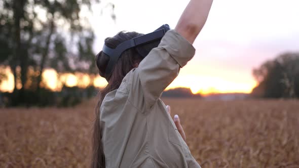 Beautiful Girl in a Golden Wheat Field Uses Virtual Reality Glasses in the Sunset