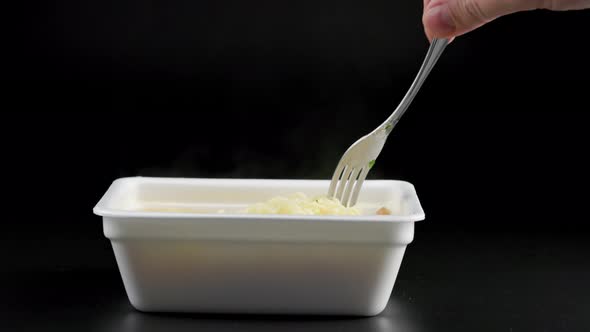 Bare Caucasian Hand with Fork Stirring Freshly Cooked Instant Noodle in Styrofoam Bowl on Black
